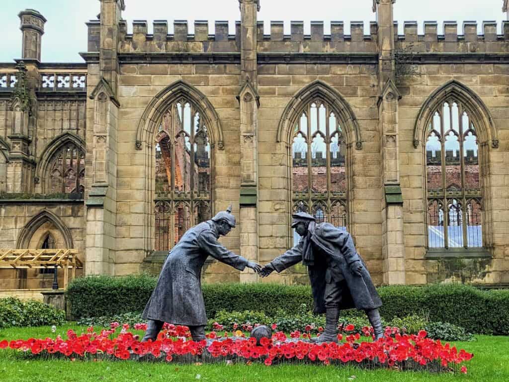statue of WWI soldiers shaking hands at bombed out church in liverpool with poppies
